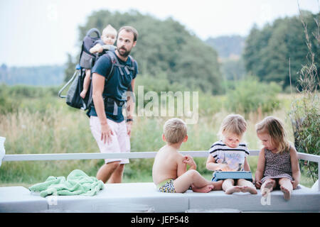 Kinder spielen mit digital-Tablette im Garten, Vater auf Hintergrund Stockfoto