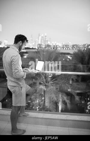 Mann mit Laptop auf der Terrasse, Stadtbild auf Hintergrund Stockfoto