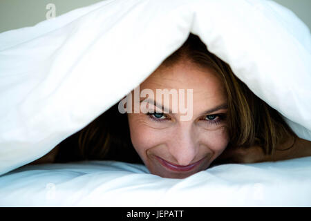 Frau peering Out unter ihrer Bettdecke Stockfoto