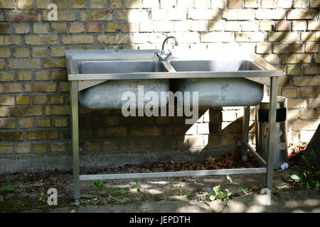 Eine alte Geschirrspülmittel Becken auf vier Beinen steht außerhalb an einer Hauswand. Stockfoto