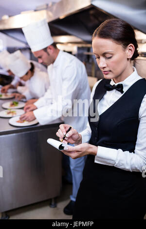 Kellnerin mit Notizen in der gewerblichen Küche Stockfoto