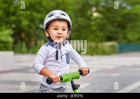 Kind Junge im weißen Helm auf seinem ersten Fahrrad mit Helm fahren. Fahrrad ohne Pedale. Stockfoto