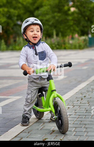 Kind Junge im weißen Helm auf seinem ersten Fahrrad mit Helm fahren. Fahrrad ohne Pedale. Stockfoto