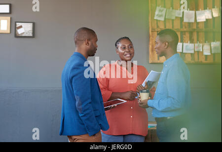 Lässig gekleidet drei junge afrikanische Büro Kollegen lächelnd und miteinander reden, während Sie stehen in einem großen modernen Büro Stockfoto