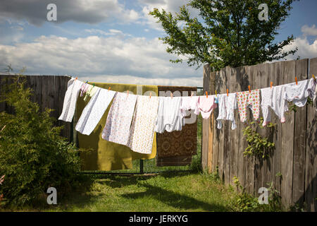 Bettwäsche und Kleidung trocknen auf das Seil bei gutem Wetter im Sommer. Kinderbekleidung und Windeln hängen unter freiem Himmel im Innenhof Stockfoto