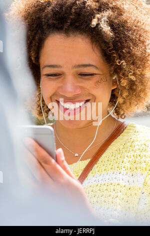 Aufnahme einer Frau mit einem Smartphone hautnah. Sie trägt Kopfhörer und lächelnd auf den Bildschirm. Stockfoto