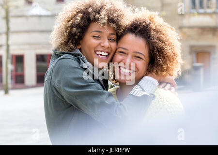 Zwei Freundinnen umarmen und Lächeln für die Kamera in der Stadt. Stockfoto