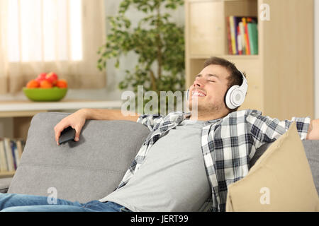 Einzelner legerer Mann mit Augen geschlossen Musikhören auf Linie über ein Smartphone sitzen auf einem Sofa im Wohnzimmer in einem Haus-Interieur Stockfoto