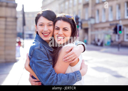 Zwei Freundinnen umarmen in der Stadt. Sie sind in die Kamera schaut und lächelt. Stockfoto