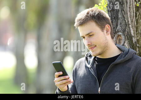 Ernsthafte teenboy mit einem smart-Phone auf Linie im freien stützte sich auf einen Baum in einem park Stockfoto