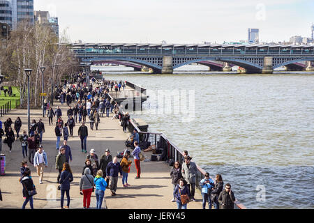 LONDON, UK - 6. April 2017: Touristen gehen auf den von Bäumen gesäumten Weg auf der Southbank des Flusses Themse an einem sonnigen Frühlingstag Stockfoto