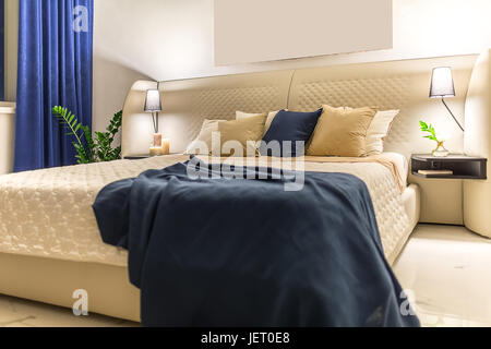 Helle moderne Schlafzimmer mit weißen Wänden und Licht gefliesten Boden. Es ist ein Beige Bett mit bunten Kissen und ein blaues Karomuster, Regale mit Kerzen Stockfoto