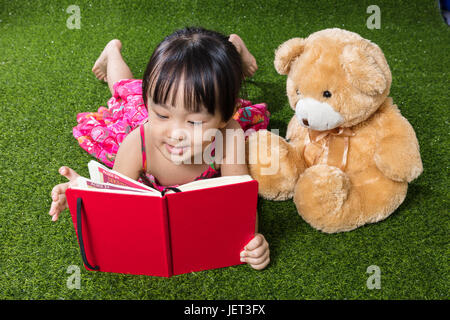 Asiatische chinesische Mädchen auf dem Rasen liegen und Buch mit Teddybär im Outdoor-park Stockfoto