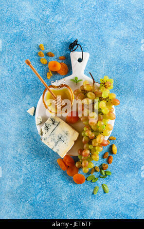 Reife Trauben, Gorgonzola-Käse, Honig und getrocknete Früchte auf einem weißen Marmor-Board. Sommer raffiniert leichten Snack auf blauem Hintergrund Stockfoto