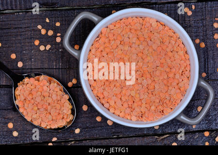 Rote Linsen in einem Metalllöffel und Keramiktopf auf Holztisch Stockfoto