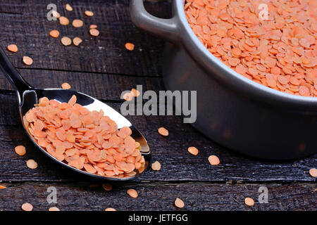 Rote Linsen in einem Löffel und in einem Keramiktopf auf Holztisch Stockfoto