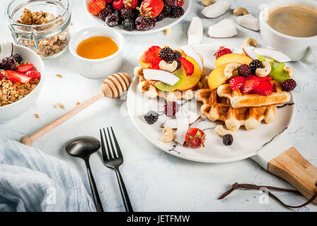 Frühstück. Hausgemachte frische belgische weiche Waffeln mit Honig, frischem Obst, Nüssen und Beeren; Joghurt mit Müsli und Obst, eine Tasse Kaffee. Leichte Konz Stockfoto