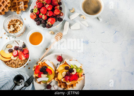Frühstück. Hausgemachte frische belgische weiche Waffeln mit Honig, frischem Obst, Nüssen und Beeren; Joghurt mit Müsli und Obst, eine Tasse Kaffee. Leichte Konz Stockfoto