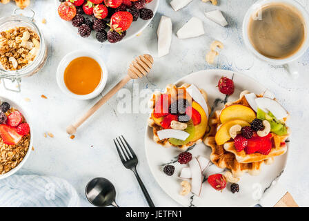 Frühstück. Hausgemachte frische belgische weiche Waffeln mit Honig, frischem Obst, Nüssen und Beeren; Joghurt mit Müsli und Obst, eine Tasse Kaffee. Leichte Konz Stockfoto