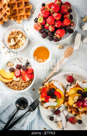 Frühstück. Hausgemachte frische belgische weiche Waffeln mit Honig, frischem Obst, Nüssen und Beeren; Joghurt mit Müsli und Obst, eine Tasse Kaffee. Leichte Konz Stockfoto