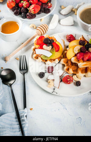 Frühstück. Hausgemachte frische belgische weiche Waffeln mit Honig, frischem Obst, Nüssen und Beeren; Joghurt mit Müsli und Obst, eine Tasse Kaffee. Leichte Konz Stockfoto