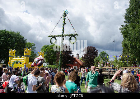 Stockholm, Schweden - 23. Juni 2017. Menschen feiern die schwedische Urlaub Mittsommer durch die Erhöhung des Maibaum bedeckt in Blüten und Blättern in Akalla, eine s Stockfoto