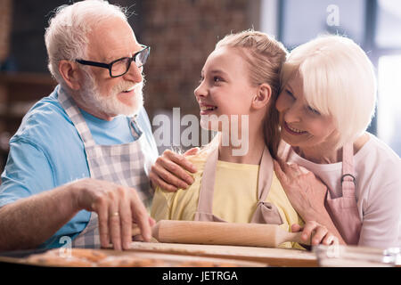 Großmutter, Großvater und Enkelin Kochen und Kneten von Teig für Kekse mit Küchenutensilien am Küchentisch, Kochen in der Küche concept Stockfoto