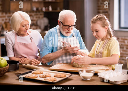 Großmutter, Großvater und Enkelin Kochen und Kneten von Teig für Kekse am Küchentisch, Kochen in der Küche concept Stockfoto