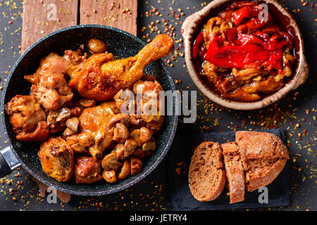 High-Angle Shot eine Pfanne mit gebratenes Huhn und Kaninchen, eine Schüssel mit spanischen Escalivada, eine Mischung aus gegrilltem Gemüse und ein Stück Brot auf Stockfoto