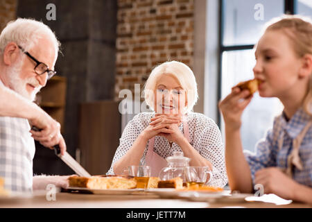 Seitenansicht der Mann schneiden hausgemachte Kuchen mit der Familie in der Nähe von Stockfoto