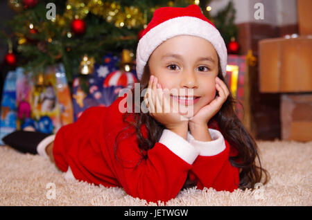 Schönes Lächeln auf den Lippen Litle Mädchen Kleidung ein Weihnachten mit einem Weihnachtsbaum-Hintergrund mit einigen Geschenken. Stockfoto