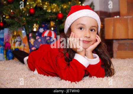 Schönes Lächeln auf den Lippen Litle Mädchen Kleidung ein Weihnachten mit einem Weihnachtsbaum-Hintergrund mit einigen Geschenken. Stockfoto