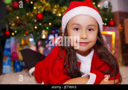 Schönes Lächeln auf den Lippen Litle Mädchen Kleidung ein Weihnachten mit einem Weihnachtsbaum-Hintergrund mit einigen Geschenken. Stockfoto