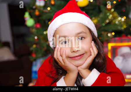 Schönes Lächeln auf den Lippen Litle Mädchen Kleidung ein Weihnachten mit einem Weihnachtsbaum-Hintergrund mit einigen Geschenken. Stockfoto