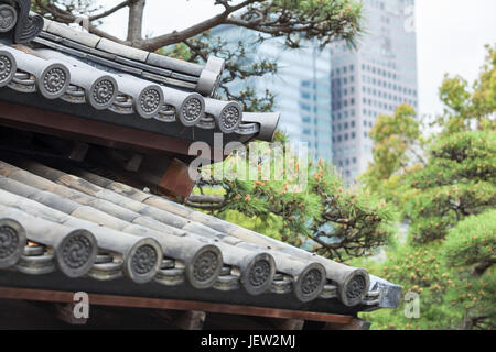 Teil des alten traditionellen japanischen Dach gegen immergrüne Kiefern und zeitgenössische Gebäude im Hintergrund Stockfoto