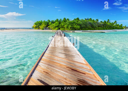 Holzsteg in Richtung einer kleinen Insel im Indischen Ozean, Malediven. Sonnigen blauen Himmel. Stockfoto