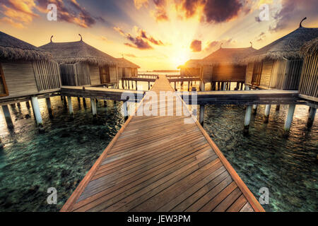 Holzsteg in Richtung Wasser-Villen. Resort auf den Malediven Insel im Indischen Ozean bei Sonnenuntergang Stockfoto