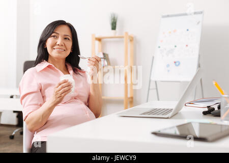Positive Schwangere Essen Joghurt im Büro Stockfoto