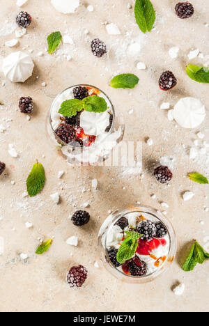 Traditionelle englische Dessert. Eton Mess - Sahne, Baiser, frische Brombeeren, Sauce und Karamell. Gläser auf einem Leuchttisch Stein zu dienen. Co Stockfoto