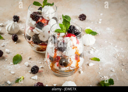 Traditionelle englische Dessert. Eton Mess - Sahne, Baiser, frische Brombeeren, Sauce und Karamell. Gläser auf einem Leuchttisch Stein zu dienen. Co Stockfoto