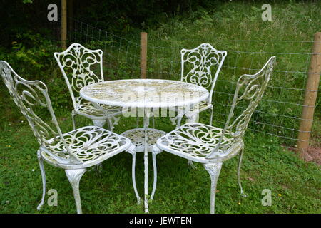 Verwitterte verzierten gescrollt Aluminium weiss lackiert runder Tisch und Stuhl, der auf Rasen mit Drahtgeflecht Grenze zaun weide Gras im Hintergrund Stockfoto