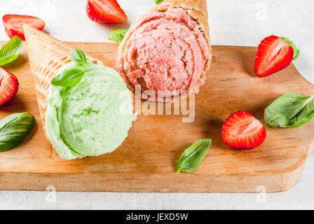 Sommer frische Desserts. Grüne Basilikum und roten Erdbeereis in einem Kegel. Auf einem weißen Stein Tisch mit Basilikum und frischen Erdbeeren um. Auf Stockfoto