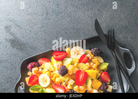 Vegane diätetische Lebensmittel. Vitamine. Dessert. Sommer. Salat aus frischen Bio-Obst Mango, Pfirsich, Apfel, Banane, Kiwi, Erdbeeren, Brombeeren. Auf schwarzen ce Stockfoto