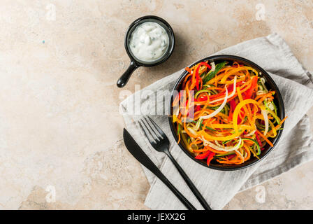 Vegane Ernährung, Diät. Salat von rohem Gemüse Nudeln, Teigwaren aus Karotten, Zucchini, Paprika. In portionierten schwarz Schüssel mit Joghurt-Sauce auf eine Registerkarte "Stein" Stockfoto