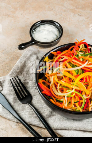 Vegane Ernährung, Diät. Salat von rohem Gemüse Nudeln, Teigwaren aus Karotten, Zucchini, Paprika. In portionierten schwarz Schüssel mit Joghurt-Sauce auf eine Registerkarte "Stein" Stockfoto