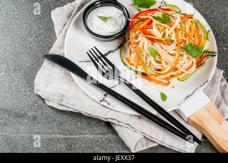 Vegane Ernährung, Diät. Einen warmen Salat, Reis Nudeln garnieren und rohe Gemüse Nudeln, Karotten einfügen, Zucchini, Paprika. Auf weiße Marmorplatte auf eine Registerkarte "Stein" Stockfoto