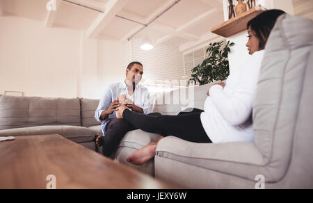 Mann massiert seine schwangere Frau Beine zusammen aufs Sofa setzt. Mann, Fußmassage, schwangere Frau zu Hause zu geben. Stockfoto