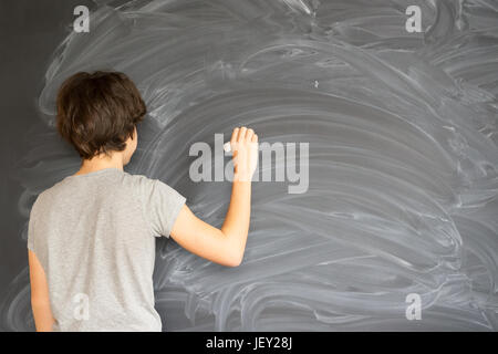 Teenager Boy mit Kreide in der hand auf leere Tafel schreiben Stockfoto