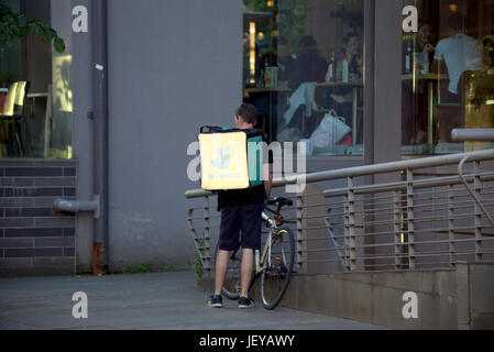 junger Mann Junge Lieferung Fahrrad Radfahrer Deliveroo Essen Lieferung SMS warten auf Arbeit liefern vor restaurant Stockfoto