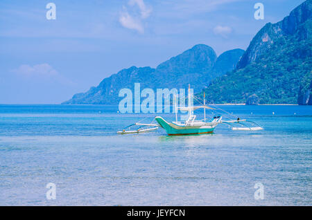 Weiße Banca Boot im ruhigen blauen Ozean, sieben Commandos Strand im Hintergrund, El Nido, Philippinen. Stockfoto